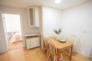 A room with a wooden dining table, white chairs, a small cabinet, and a white door leading to another room. - Airport Cozy 2 Bedroom Suite & Separate Entrances & Full kicthen (Richmond)
