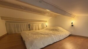 A bedroom with a bed, wooden flooring, a sloped ceiling, and two wall-mounted lights. - Quiet studio apartment (Aspremont)