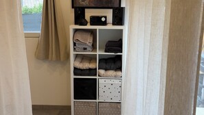A narrow hallway with an air conditioning unit, a painting on the wall, and a storage unit with folded blankets. - Quiet studio apartment (Aspremont)