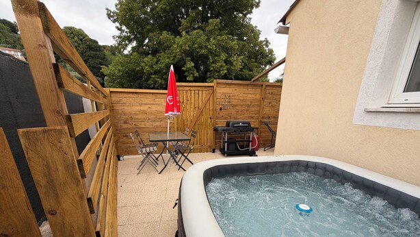 A hot tub with a wooden deck, a table with chairs, and a barbecue grill. - Quiet studio apartment (Aspremont)