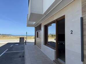 A building with a number '2' on the wall, a paved area with a drainage grate, and a view of the sea. - Flower Beach Helgueras 2 - 6092 (Noja)