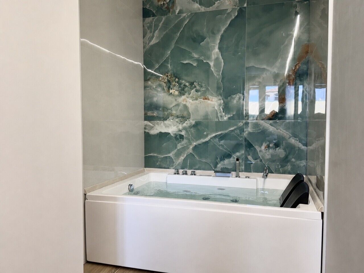 Une salle de bain moderne avec un mur en marbre, une baignoire blanche et le reflet d’un immeuble que l’on peut voir.