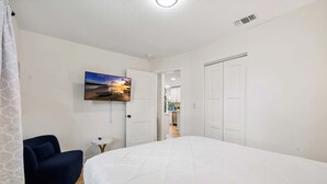 A bedroom with a large bed, a TV mounted on the wall, a chair, and a door leading to a bathroom. - Cozy Ridge Manor Retreat - SUMMER SPECIAL (Ridge Manor)