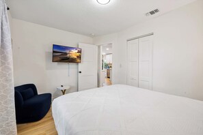 Ein Schlafzimmer mit einem großen Bett, einem an der Wand montierten Fernseher, einem Sessel und einer Tür zu einem Badezimmer.