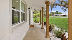 A covered porch with a concrete floor, wooden pillars, and a view of a grassy yard with a house in the background. - Cozy Ridge Manor Retreat - SUMMER SPECIAL (Ridge Manor)