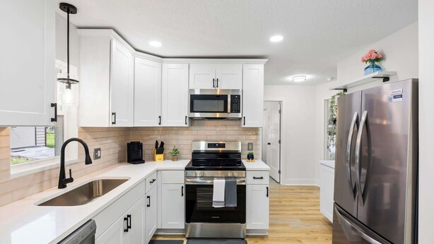 A modern kitchen with white cabinetry, stainless steel appliances, a dishwasher, and a black faucet. - Cozy Ridge Manor Retreat - SUMMER SPECIAL (Ridge Manor)