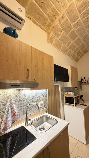 A compact kitchen with a built-in stove, a sink, and a television mounted on the wall. - Vacation rental in the historic center of Trani (Trani)
