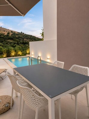 An outdoor pool area with a table and chairs, surrounded by a white wall and a view of a hilly landscape. - Oceana Suites Villas Deluxe Private Pool Studio (Apokoronas)