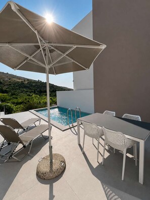 An outdoor pool area with a table and chairs, a sun umbrella, and a view of the landscape. - Oceana Suites Villas Deluxe Private Pool Studio (Apokoronas)