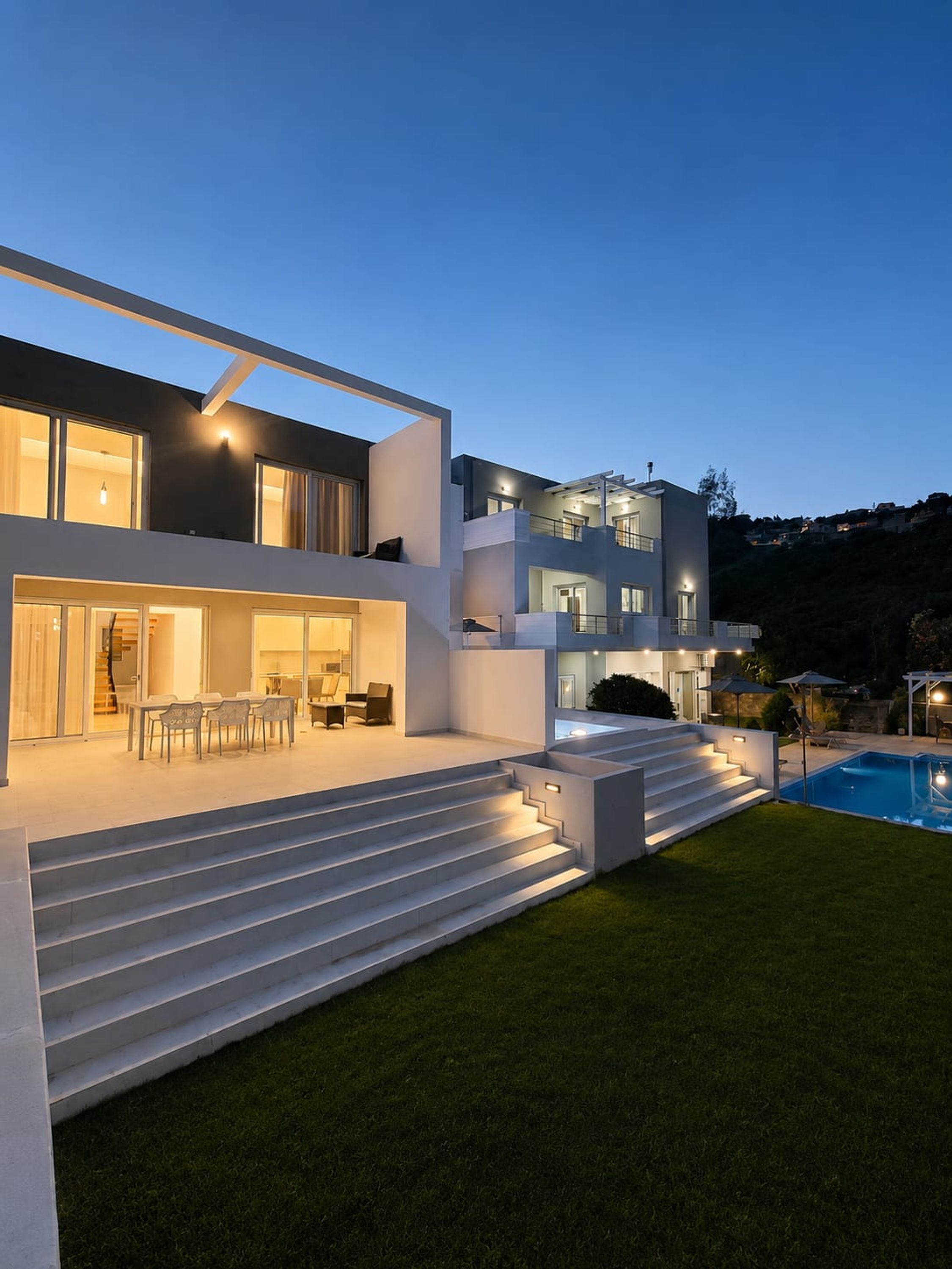 A modern two-story house with a swimming pool, outdoor seating, and a well-lit staircase.