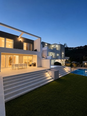 Ein modernes, zweistöckiges Haus mit Swimmingpool, Außenbereich und einer gut beleuchteten Treppe.