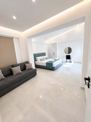 Ein modernes Schlafzimmer mit Bett, Sofa, Sessel und Spiegel.