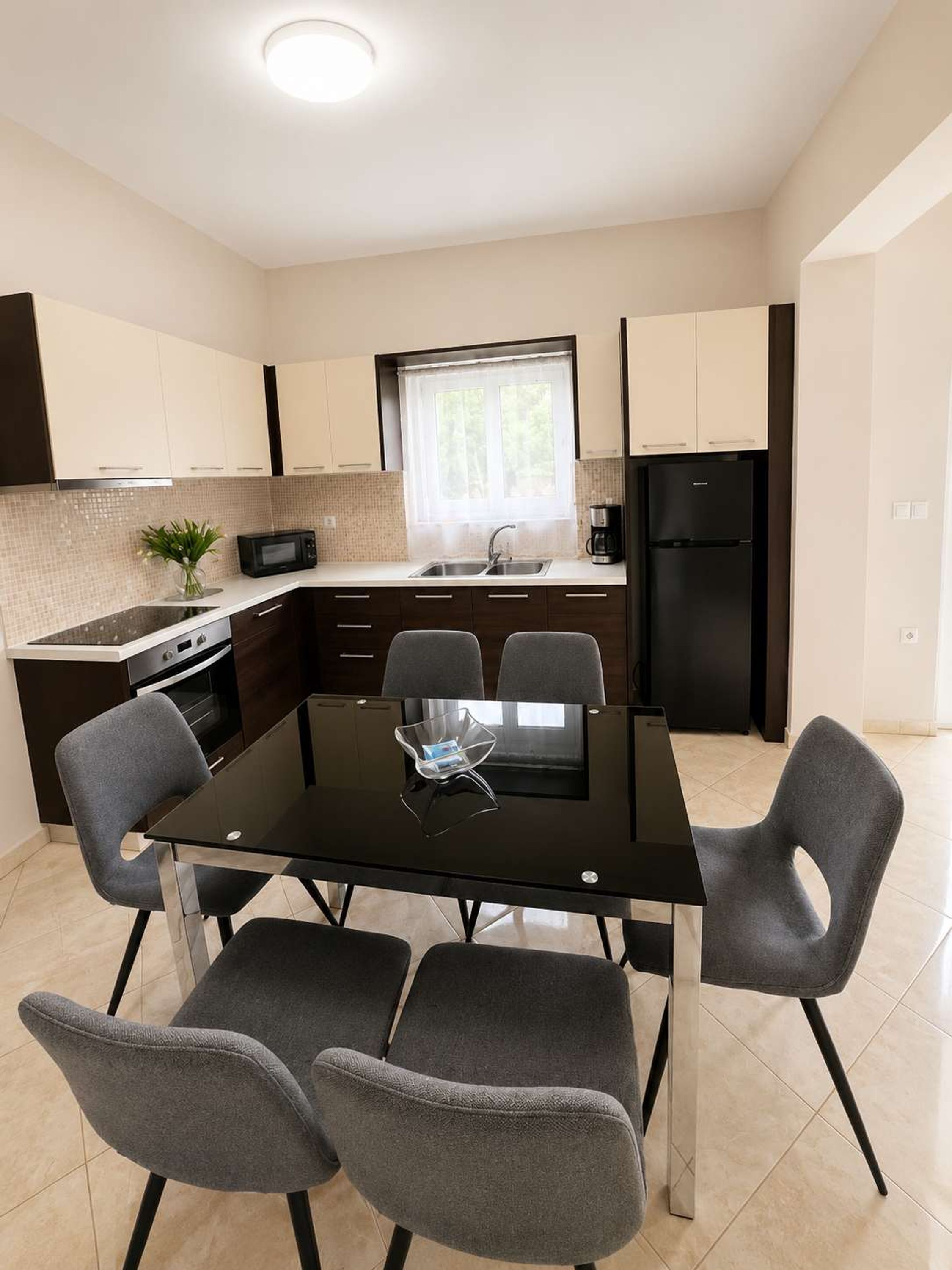 A modern kitchen with a dining table, chairs, a refrigerator, and a microwave.