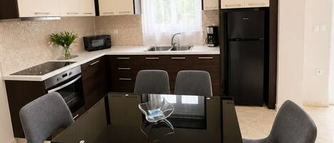 A modern kitchen with a dining table, chairs, a refrigerator, and a microwave.