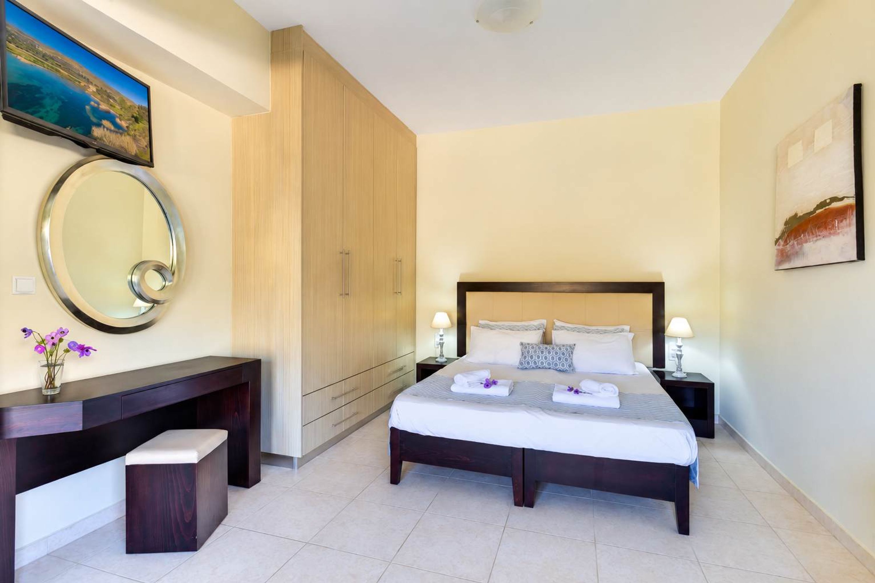 Une chambre d’hôtel comprenant un lit, des tables de chevet, un bureau, un miroir et des œuvres d’art accrochées aux murs.