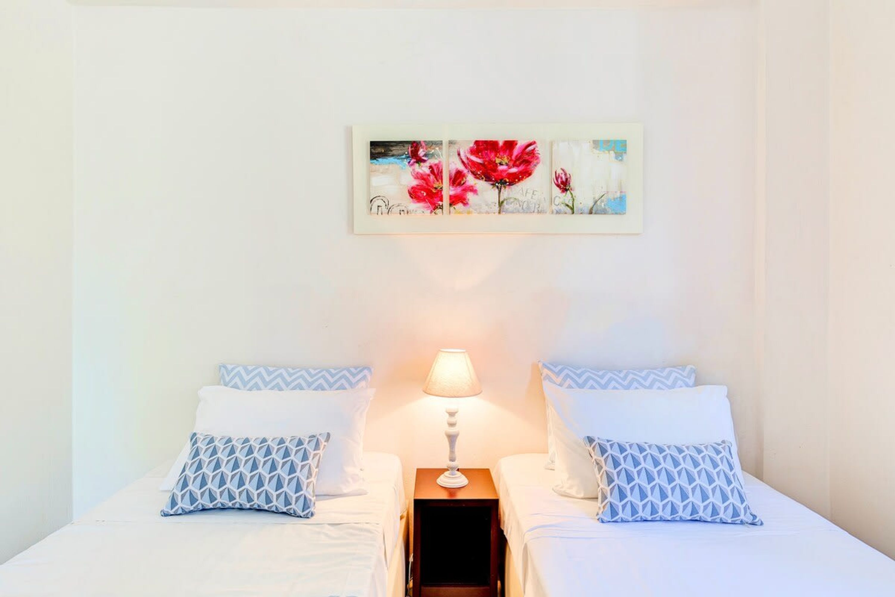 Una camera d'albergo con due letti, un comodino con una lampada e un quadro appeso al muro.