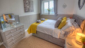 Une chambre à coucher comprenant un lit, une commode, une fenêtre avec des rideaux, un tableau décoratif et une lampe de chevet.