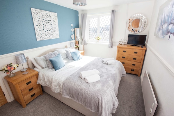 A bedroom with a bed, bedside tables, a dresser, a TV, and decorative wall art.