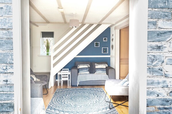 A room with a blue accent wall, a grey sofa, a white chair, a patterned rug, and a staircase.
