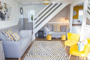 A living room with a sofa, armchairs, a patterned rug, a staircase, and a kitchen area.