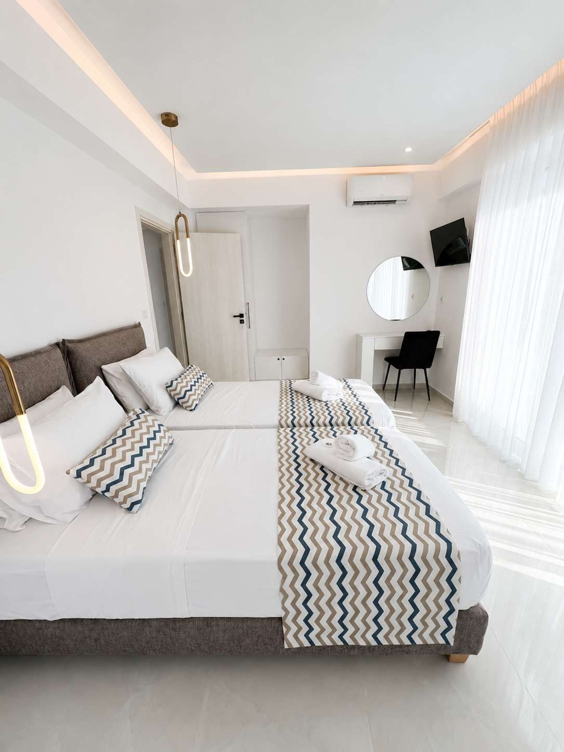 Une chambre d’hôtel moderne avec un grand lit, une table de chevet, une chaise, un miroir rond et un téléviseur.