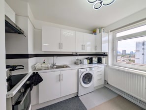 Eine kleine Küche mit Waschmaschine, Spüle und Fenster mit Blick auf die Stadt.