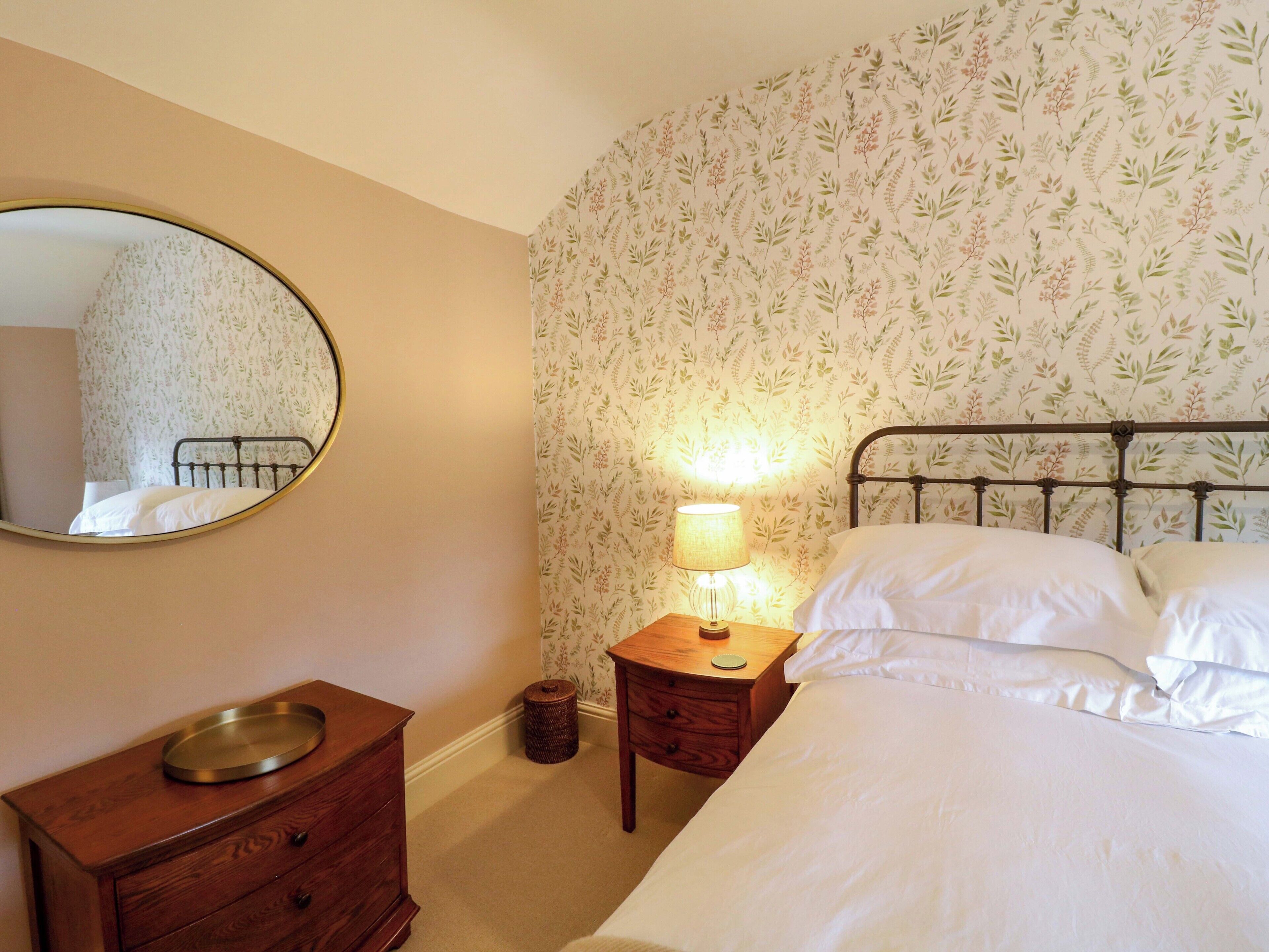 A bedroom with a bed, a bedside table with a lamp, a dresser, and a mirror on the wall.