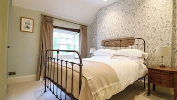 Un dormitorio con una cama, una mesita de noche, un ventanal con cortinas y una pared con estampado floral.