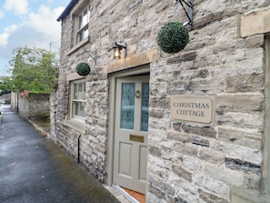 A stone building with a 'Christmas Cottage' sign, a door with glass panels, and a small hanging plant. - Christmas Cottage (Bakewell)