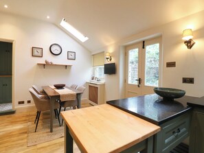 A modern kitchen with a wooden table, a bowl on the counter, and a window with a view. - Christmas Cottage (Bakewell)