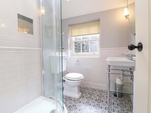 A bathroom with a glass-enclosed shower, a toilet, a sink with a mirror, and a window. - Christmas Cottage (Bakewell)