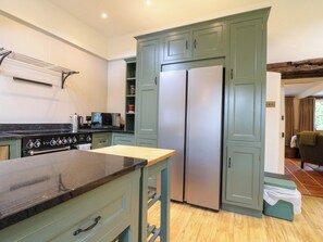 Cocina con estufa, microondas y refrigerador doble. Hay una mesa de madera y armarios con manijas.