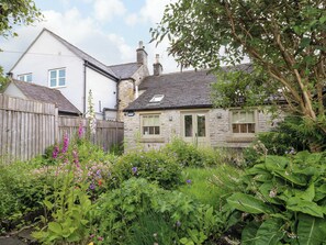 A stone house with a sloped roof, a wooden fence, and a garden with various plants and flowers. - Christmas Cottage (Bakewell)