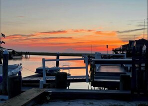 A waterfront dock with boats, a wooden pier, and a view of the sunset over the water.