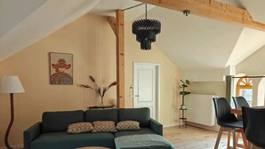 A cozy living room with a green sofa, two round wooden coffee tables, a lamp, and a hanging light fixture. - Wellness apartment: private sauna, hot tub – last-minute (Großharthau)