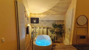 A bathroom with a bathtub, a towel rack, a mirror, and a potted plant. - Wellness apartment: private sauna, hot tub – last-minute (Großharthau)
