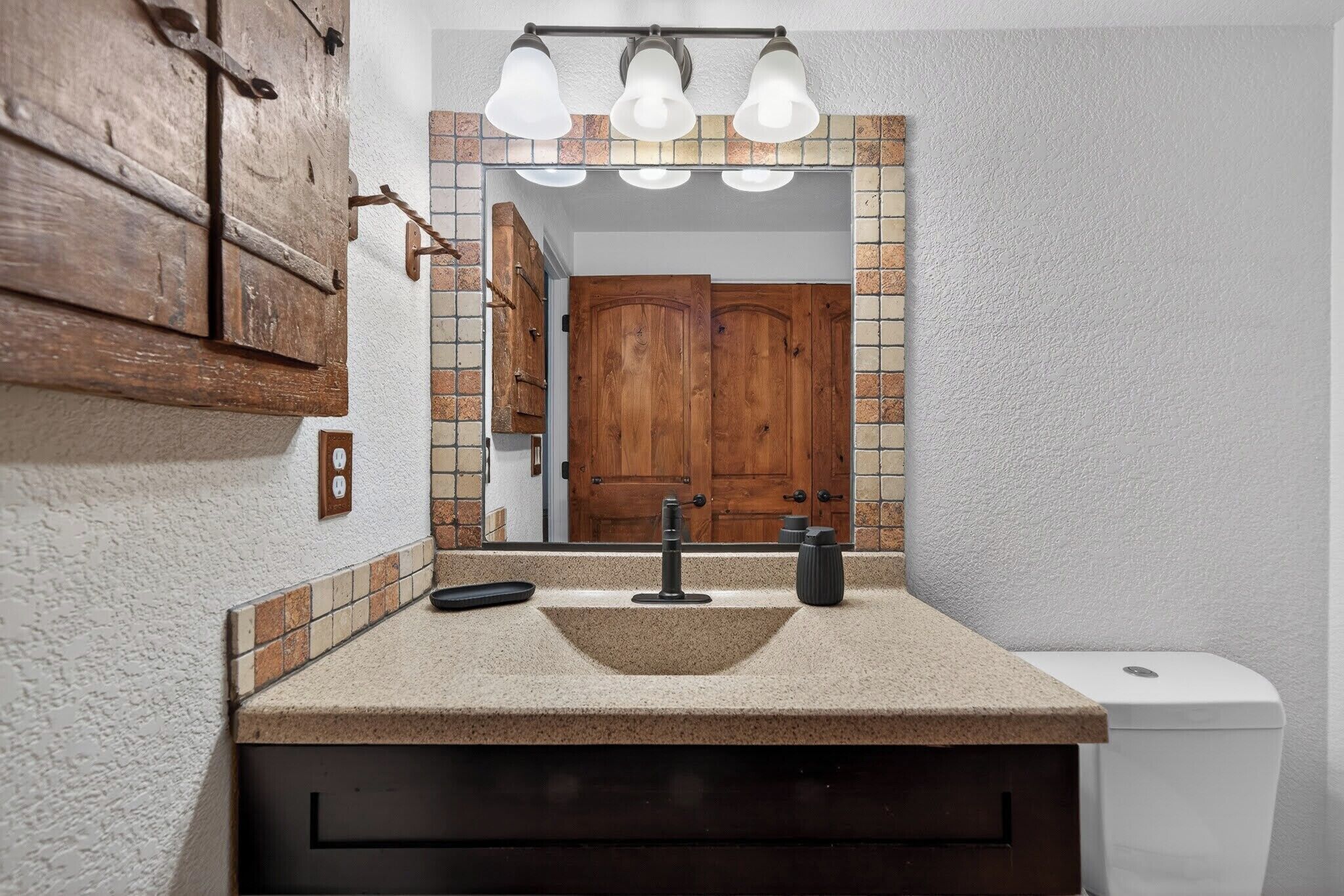 Un baño con lavamanos, espejo y puerta de madera.