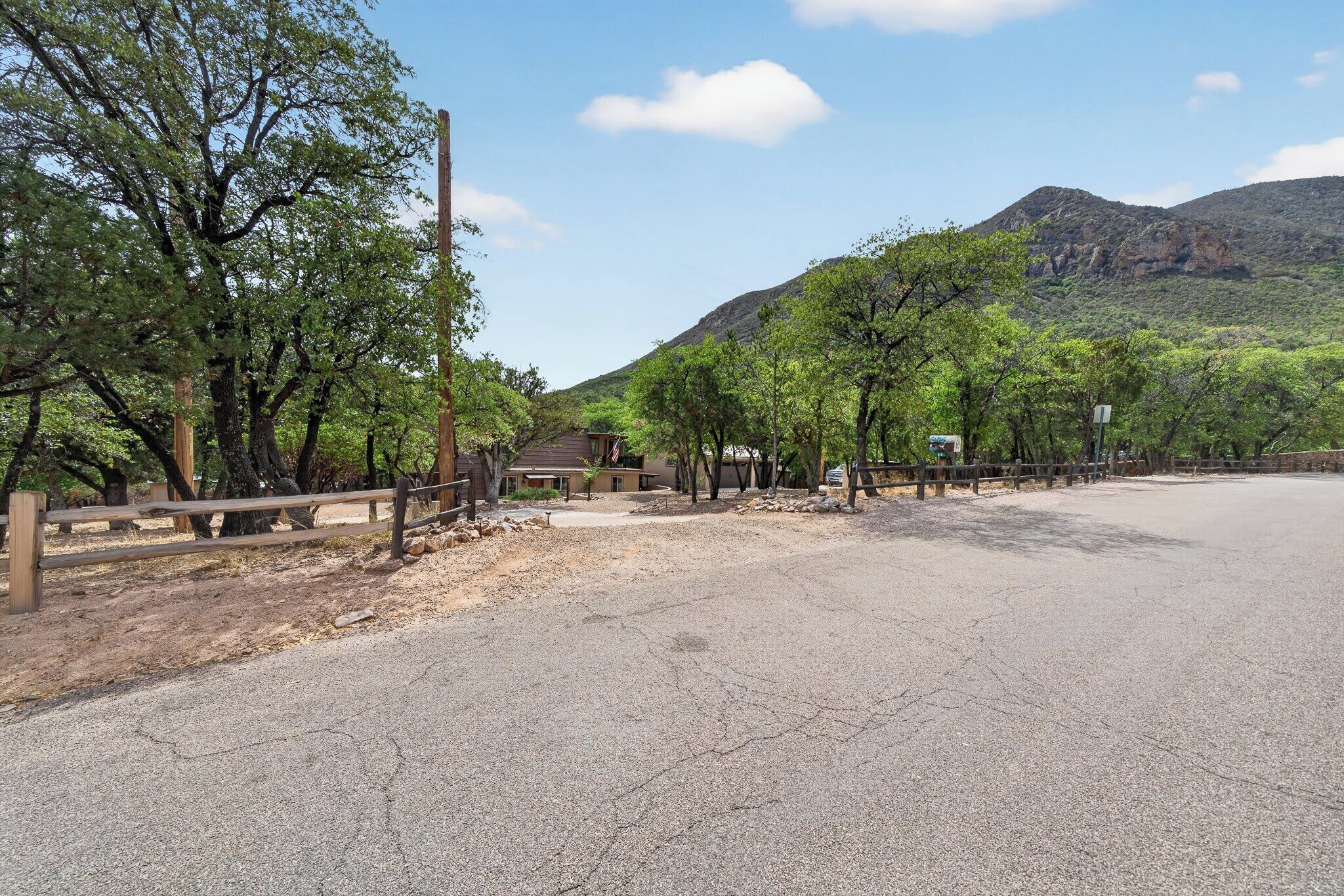 A paved road with a wooden fence, trees, and a mountain in the background.