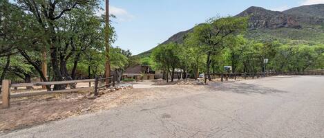 A paved road with a wooden fence, trees, and a mountain in the background.