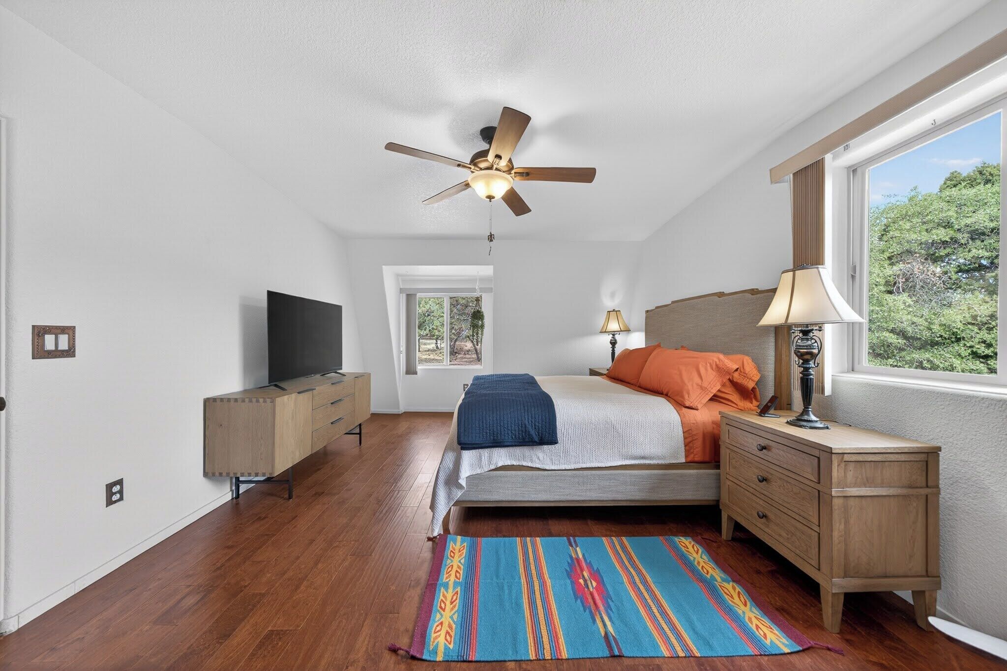 Ein Schlafzimmer mit Bett, Deckenventilator, Fernseher, Fenster und Schreibtisch.
