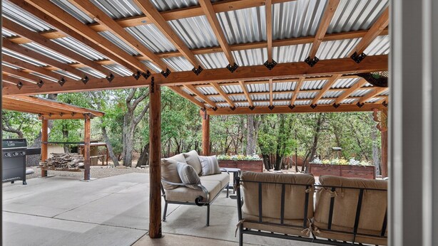 Ein überdachter Patio-Bereich mit einer Holzpergola, Gartenmöbeln und einem Grill.