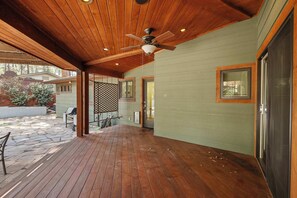 Ein überdachter Patio-Bereich mit Holzboden und Deckenventilator, eine Steinterrasse und im Hintergrund ein Haus.