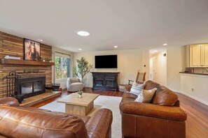 Ein Wohnzimmer mit Ledersofas, einem Kamin, einem Flachbildfernseher und Holzboden.