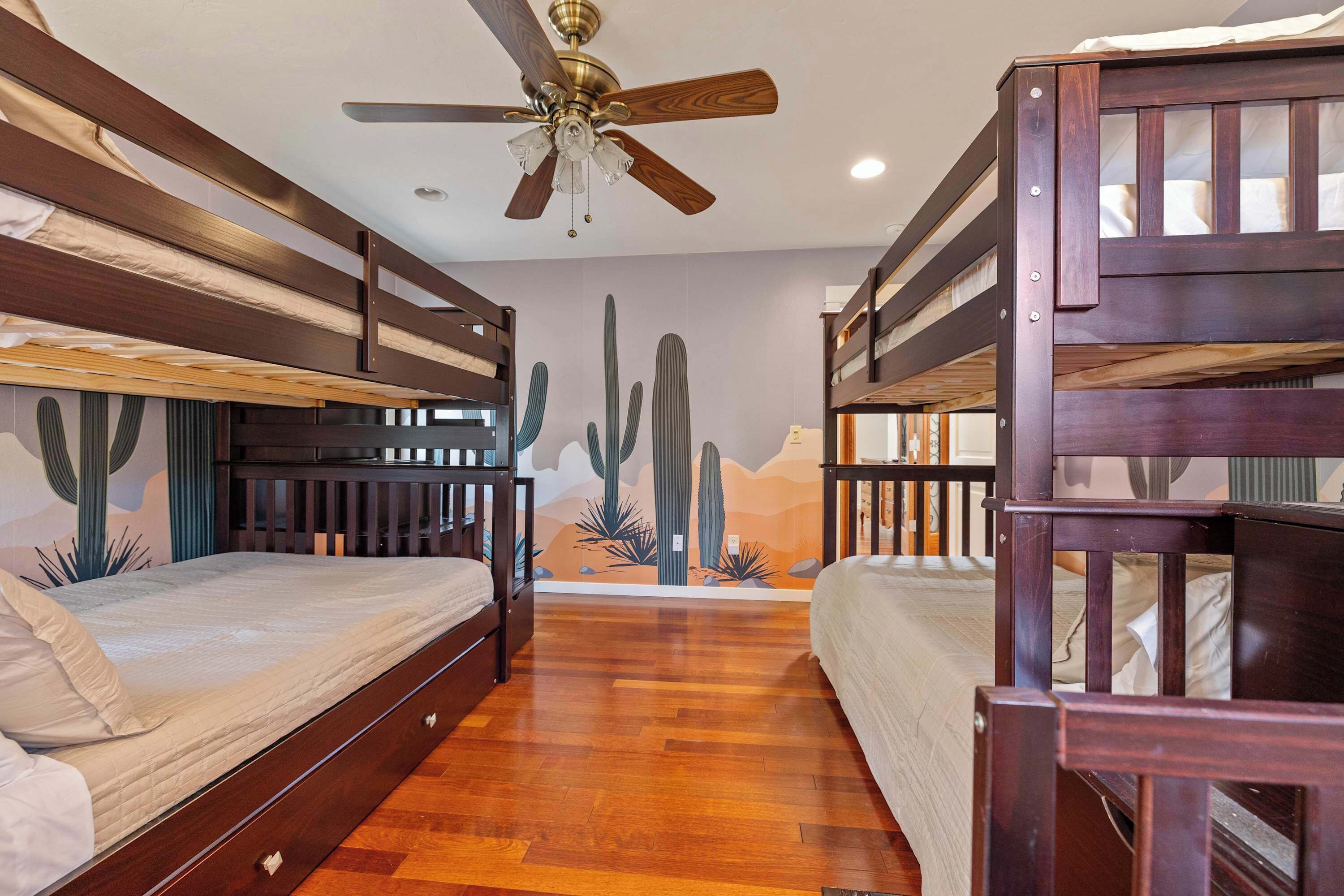 A room with bunk beds, a ceiling fan, and a cactus mural.