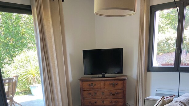 Una sala de estar moderna con un sofá, un televisor sobre un mueble de madera y una mesa de centro de vidrio.