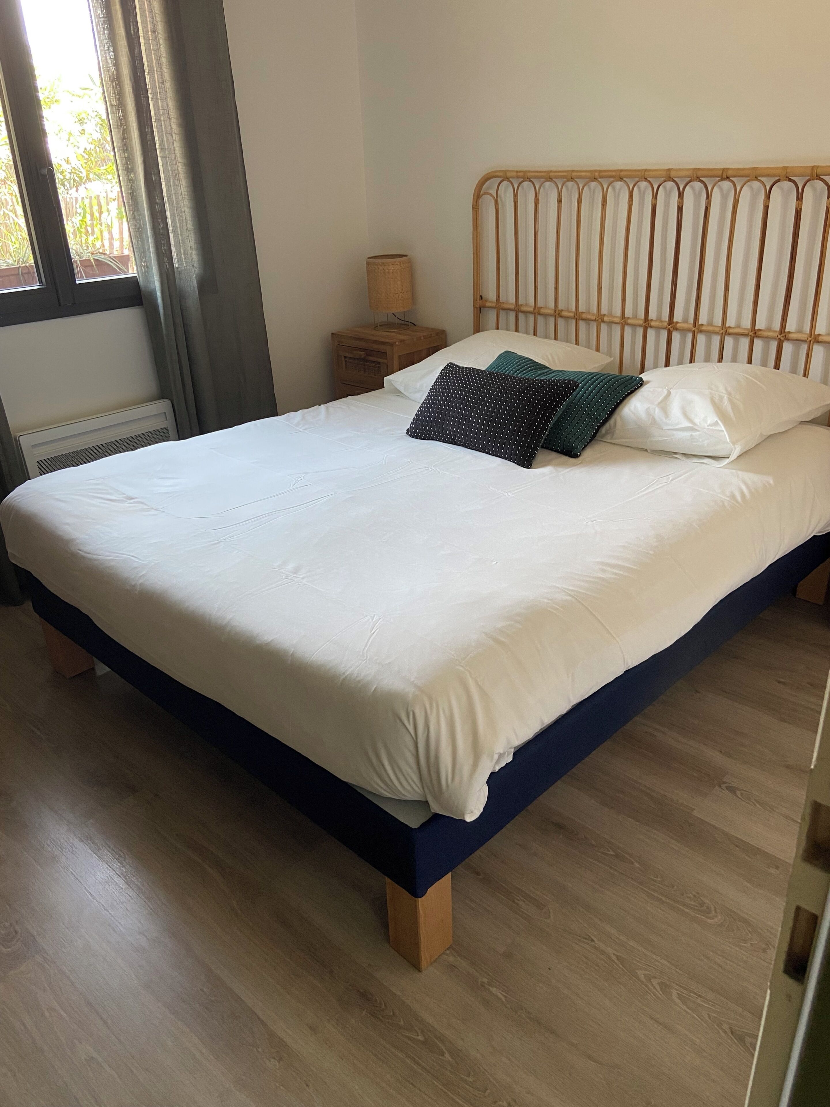 Een bed met een wit- en donkerblauwe dekbedovertrek, een houten hoofdbord en een nachtkastje met een lamp.
