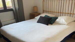 Una cama con colcha blanca y azul oscuro, un cabecero de madera y una mesita de noche con una lámpara.