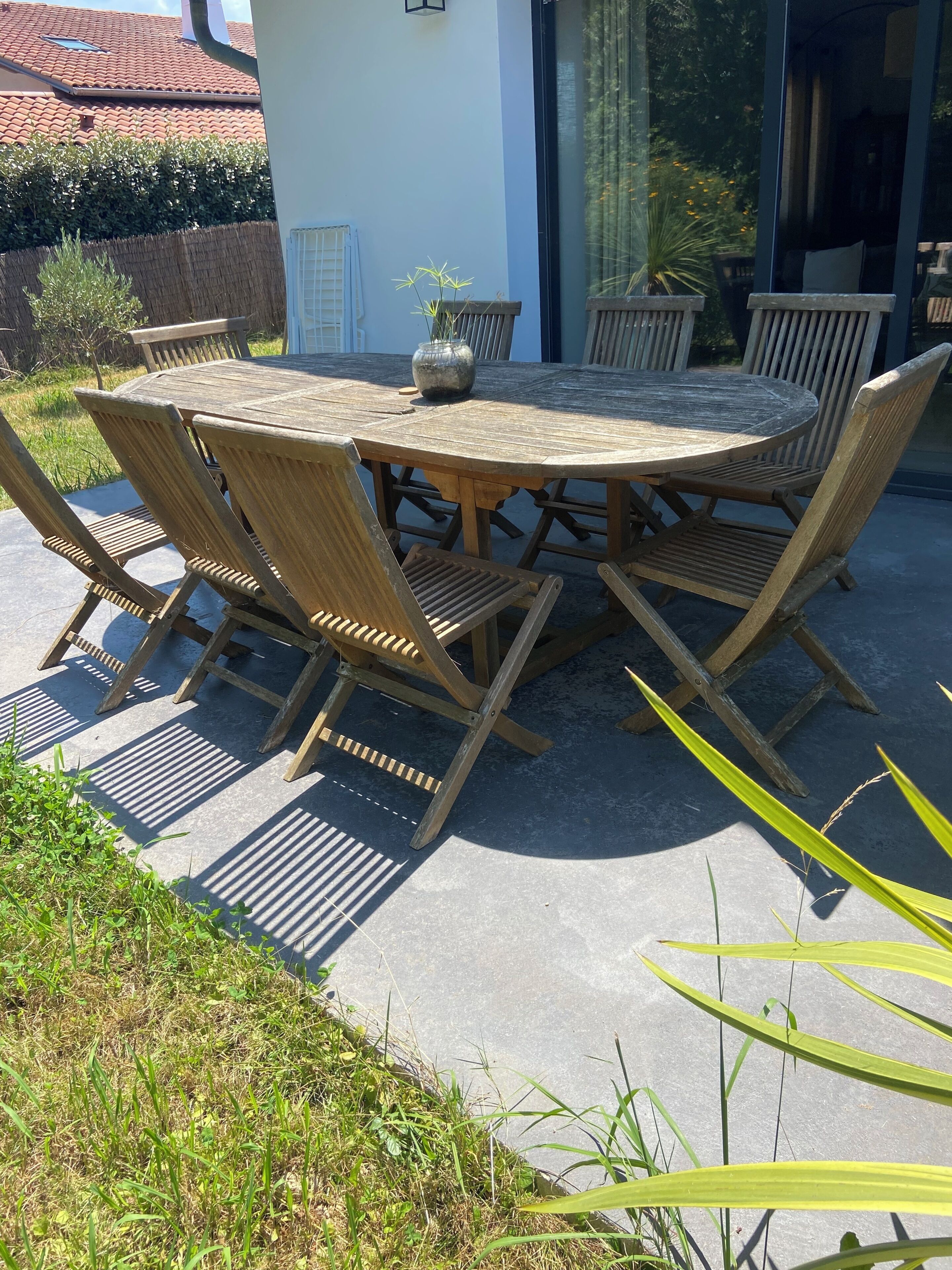 Een ronde houten tafel met stoelen, een potplant en een raam met gordijnen.