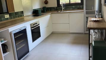 Een moderne keuken met witte kasten, een inbouwoven en een raam met uitzicht op groen.