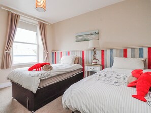 Ein Schlafzimmer mit zwei Betten, einem fensterbelaubten Fenster, einer Lampe und einem Bild an der Wand.